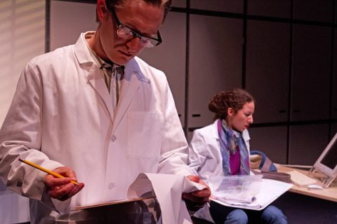 Andrew Jessop in a lab coat reviews a paper with Rae Gray